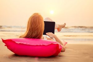 copy-space-beautiful-young-woman-working-with-laptop-on-the-tropical-beach-happy-traveling-female-using-laptop-on-holidays-lyin-down-on-pink-inflatable-mattressremote-work